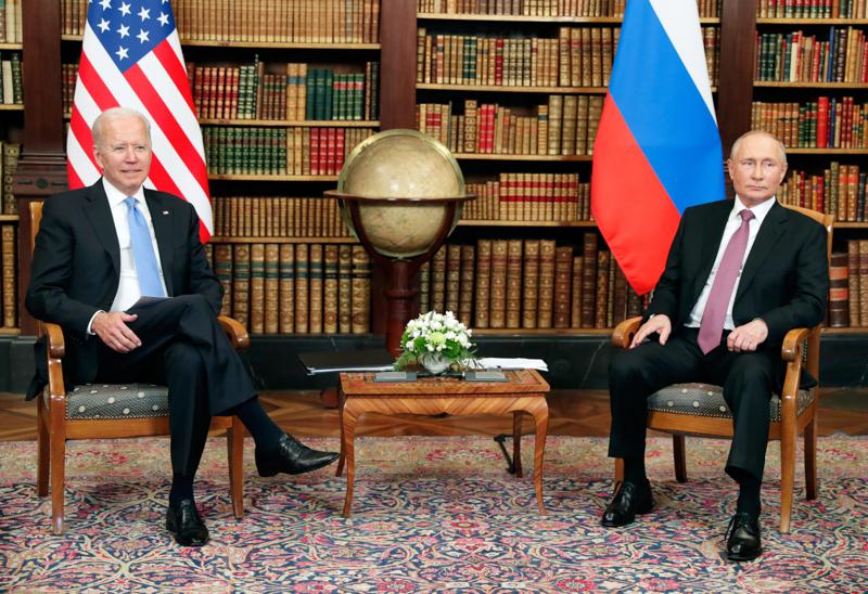 US president Joe Biden and Russian President Vladimir Putin sitting in a library next to each other with their country flags behind them and a world globe between them